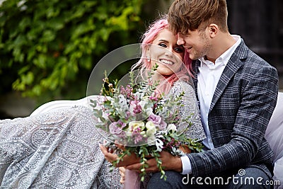 Handsome young man hugs tender woman with pink hair sitting on the white couch Stock Photo
