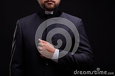 Handsome young priest with bread posing on a black background. Stock Photo