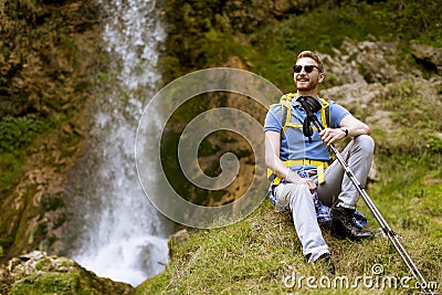 Handsome young red hair hiker stopped beside a mountain waterfall to rest Stock Photo