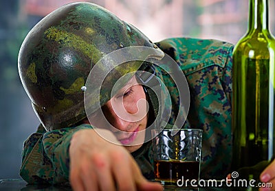 Handsome young soldier wearing uniform suffering from stress post-war, with a glass of ron and bottle next to him, in a Stock Photo