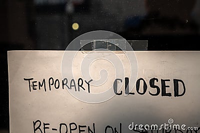 A handwritten temporarily closed sign on a white piece of paper taped to a business storefront glass window or door shut down due Stock Photo