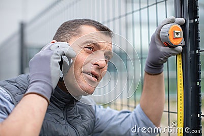 handy man measuring metal fence while calling on phone Stock Photo