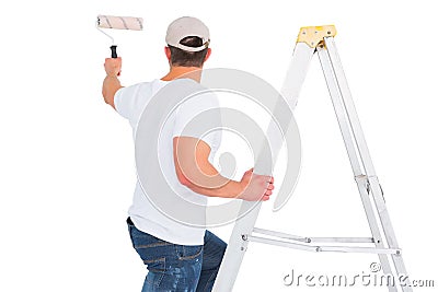 Handyman climbing ladder while using paint roller Stock Photo