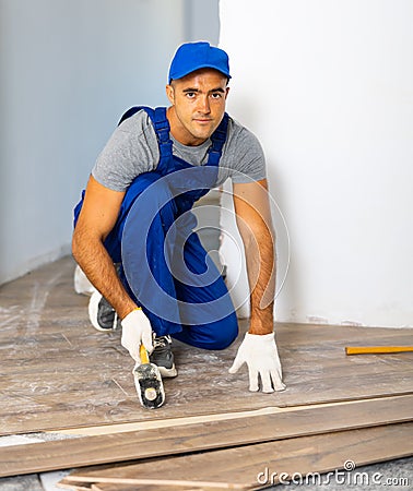 Handyman worker in work clothes use rubber hammers installing laminate panel in apartment Stock Photo