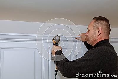 Handyman working using brad nail gun to Crown Moulding on white wall cabinets framing trim, Stock Photo