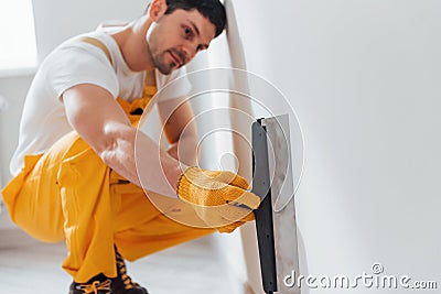 Handyman in yellow uniform polishing wall indoors. House renovation conception Stock Photo
