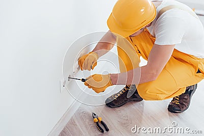 Handyman in yellow uniform works with electricity and installing new socket. House renovation conception Stock Photo