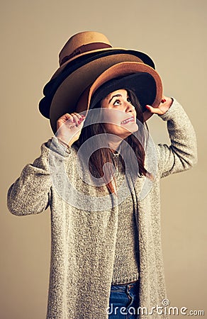 Hang on to your hats. Sale season is coming. Studio shot of a young woman wearing a pile of hats against a brown Stock Photo