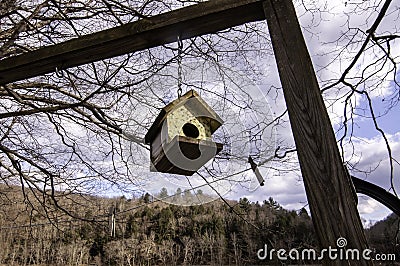 A hanging birdhouse with bare trees and bright white clouds behind it Stock Photo