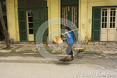 Hanoi, Vietnam - April 13, 2014: Unidentified vendor goes home with the empty baskets over old house on Hanoi str, Vietnam Editorial Stock Photo