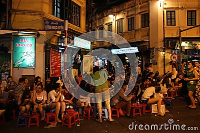 A crowded street corner in the old quarter of the city of Hanoi with young people enjoying Bia Hoi aka Editorial Stock Photo