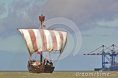 Hanseatic cog under sail with port facilities and cranes Stock Photo