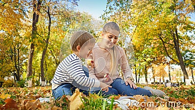 Happ family sitting on fallen yellow leaves at autumn park and eating apples Stock Photo