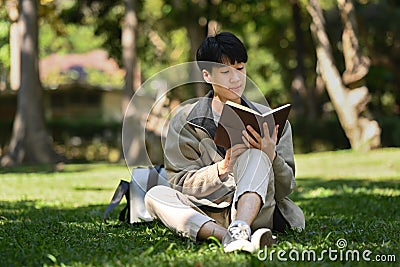 Happ young asian man reading interesting book while while sitting on green grass at sunny beautiful day Stock Photo