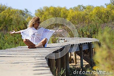 Happiness and freedom. One happy and free woman sitting alone on a wooden pier at the park opening arms and enjoying feeling. Stock Photo