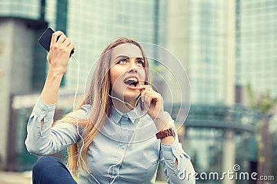 Happiness good news. woman celebrating fists up talking at phone, earphone looking up isolated near corporate business center Stock Photo