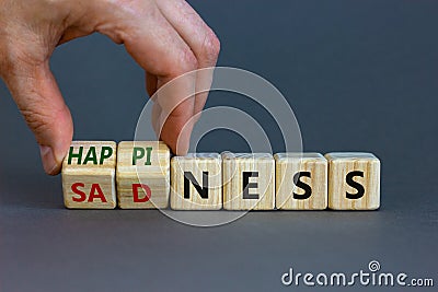 Happiness or sadness symbol. Businessman turns cubes and changes the word `sadness` to `happiness`. Beautiful grey background. Stock Photo