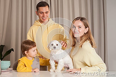Happy adorable parents in yellow sweaters with child son and white dog, three abstract plastic bottles on the table Stock Photo