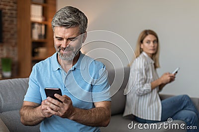 Happy adult caucasian husband with beard plays on smartphone, suffers from gadget addiction, ignores wife Stock Photo