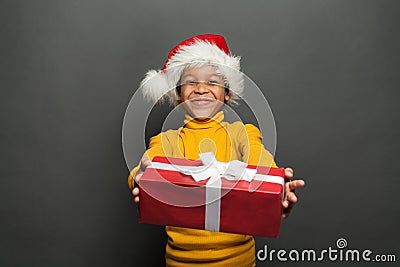 Happy African American child Santa holding red Christmas box with white silky ribbon on black background Stock Photo