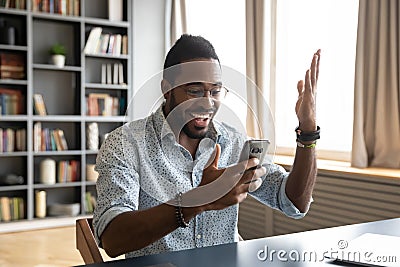 Happy African American man excited by good news, using phone Stock Photo