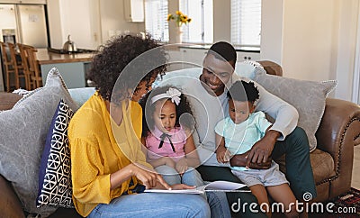 Happy African American parents with their cute children reading storybook on the sofa Stock Photo