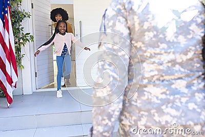 Happy african american wife and daughter welcoming male soldier outdoors with usa flag, copy space Stock Photo