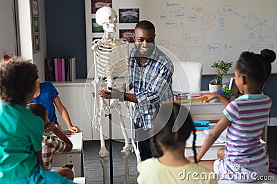 Happy african american young male teacher explaining skeleton to multiracial elementary students Stock Photo