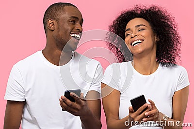 Happy african couple laughing using smartphones isolated on pink background Stock Photo