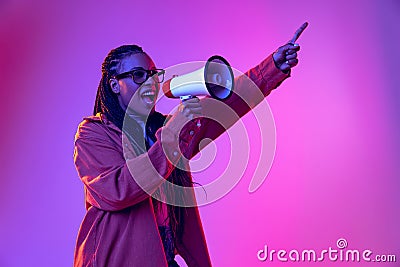 Happy african girl wearing warm shirt holding megaphone isolated on purple background in neon. Concept of emotions Stock Photo