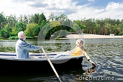 Happy aged woman touching water and her husband rowing the boat Stock Photo