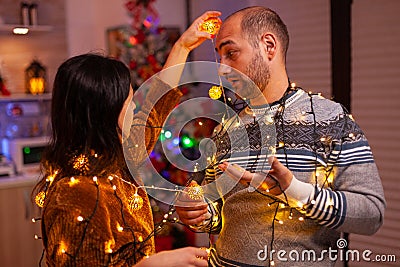 Happy amused couple stucking in christmas tree lights Stock Photo