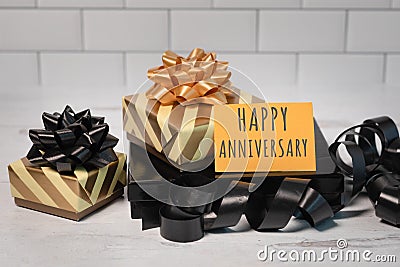 Happy anniversary greetings card sitting on gold and black wrapped gifts ribbon and bows Stock Photo