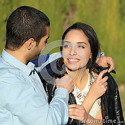 Happy arab couple flirting while man cover her with his jacket in a park Stock Photo