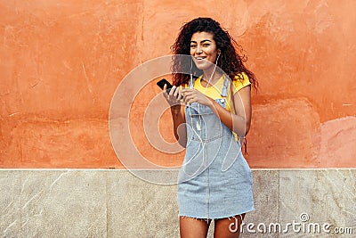 Happy Arab woman listening to music with earphones against red wall Stock Photo