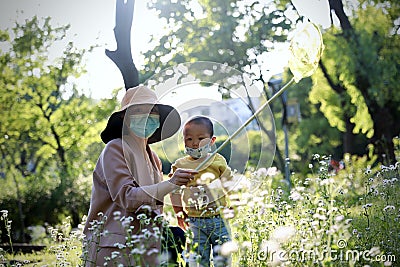 Happy Asia Chinese little boy toddler child wear mask play with his mother mom have fun hold string net catch insects childhood Stock Photo