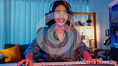 Happy asia professional girl gamer wear headphone participation play video game colorful neon lights computer in living room at Stock Photo