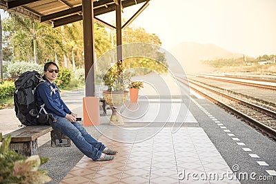 Happy asian backpack woman in casual dress sit in train station gand hold smart mobile phone Stock Photo