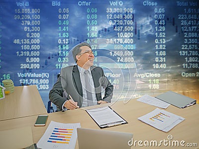 Happy asian business man sitting on his desk with stock market o Stock Photo