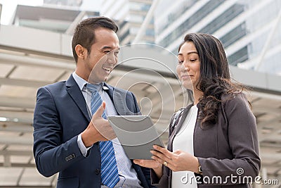 Happy Asian businessmen discussing with female boss in the city. Male open application in tablet showing data to present work Stock Photo