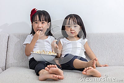 Happy Asian Chinese little sisters eating popcorn on the sofa Stock Photo