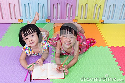 Happy Asian Chinese little sisters laying on the floor coloring Stock Photo