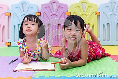 Happy Asian Chinese little sisters laying on the floor coloring Stock Photo