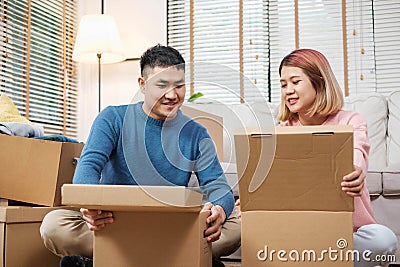 Happy asian couple open cardboard boxes while moving to new home at sofa in living room.unpacking for new house Stock Photo