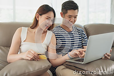 Happy asian couple shopping online using digital tablet with holding credit card and sitting on sofa at home together. Stock Photo