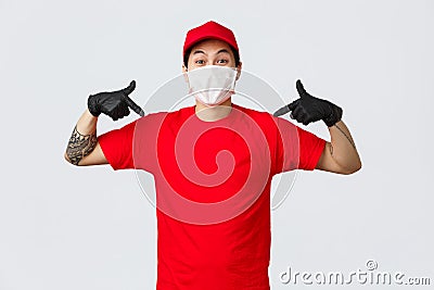 Happy asian delivery guy in red uniform, cap and t-shirt, wearing protective gloves and mask during covid19 quarantine Stock Photo