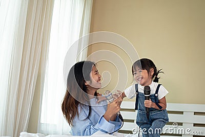 Happy Asian family loving children, kid and her sister holding microphone and singing together on bed in bedroom Stock Photo