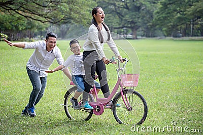 happy asian Family, parents and their children riding bike in park together. father pushes mother and son on bicycle having fun Stock Photo