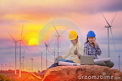 Happy Asian Female and male engineers writing the note pad on Wind turbine power generator with world map at twilight Stock Photo