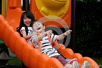 Happy asian girl and caucasian boy playing slide at school, Pre school kids at playground with happiness, Kindergarten children in Stock Photo